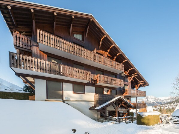 Un chalet de madera de varios pisos con balcones, con una imponente montaña nevada de fondo.