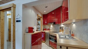 Une cuisine moderne avec des meubles de couleur rouge, des appareils électroménagers en acier inoxydable et un plafond en bois.