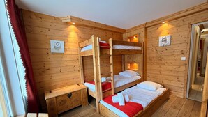 Une chambre avec un lit superposé en bois, une petite table et un banc, des murs en bois et deux tableaux encadrés accrochés aux murs.