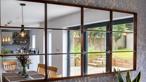 Un espace repas avec une grande fenêtre, une cuisine visible à travers cette fenêtre, et une table à manger avec des chaises.