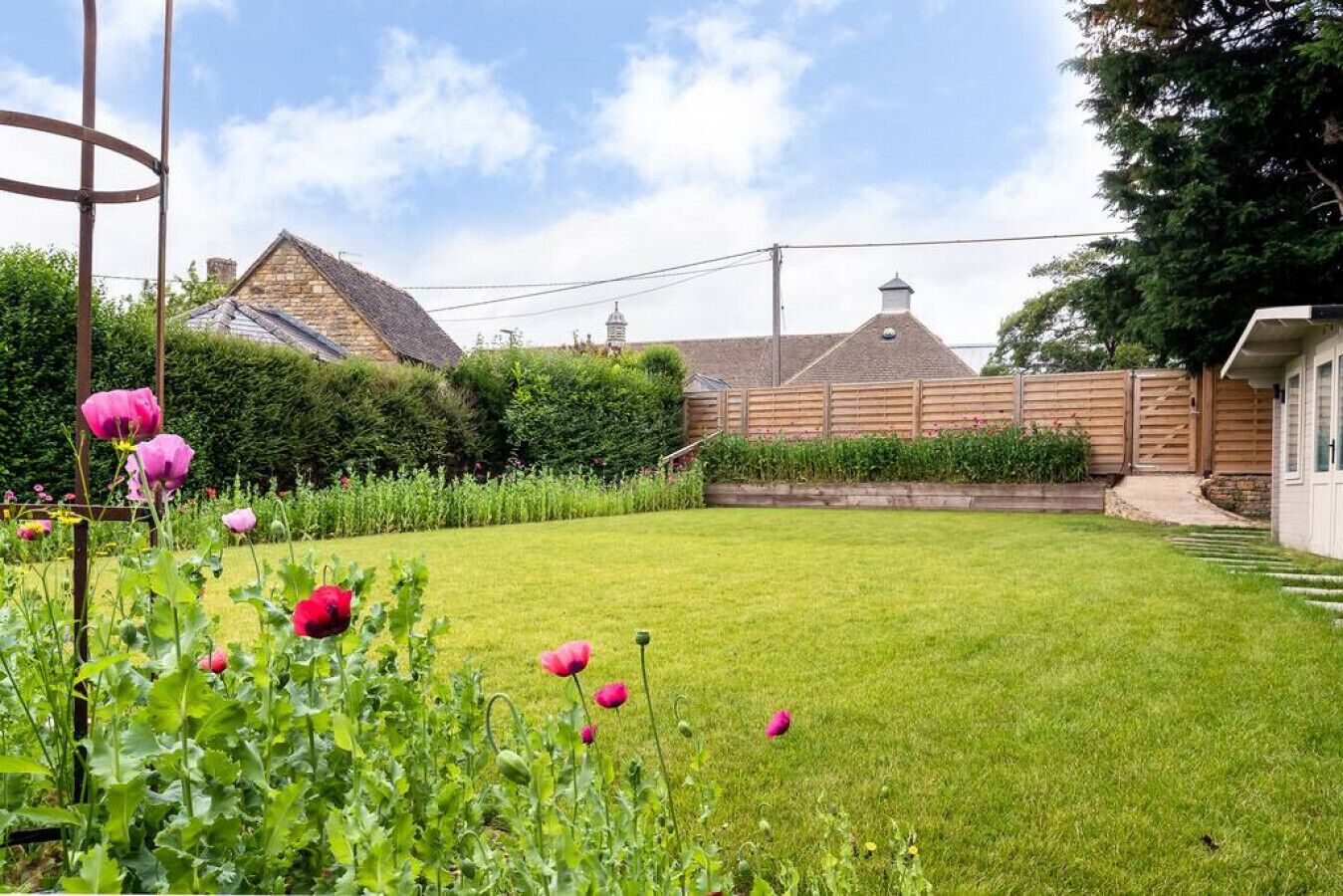 Un jardin bien entretenu, avec une pelouse, des plantes fleuries et une clôture en bois.
