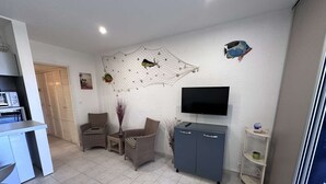 Ein modernes Wohnzimmer mit Fernseher, zwei Korbstühlen, einem kleinen Tisch mit einer Vase und einem grauen Schrank.