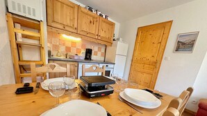 A kitchen with wooden cabinets, a dining table set with plates, glasses, and cutlery, and a grill on the table.