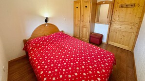 A bedroom with a wooden bed, a red floral bedspread, a wooden wardrobe, and a small red bench.