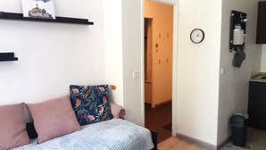 A living room with a sofa, a wall-mounted clock, and a door leading to another room.