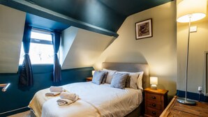 Ein Schlafzimmer mit einem Bett, Nachttischen, einer Lampe und einem Fenster mit Vorhängen.