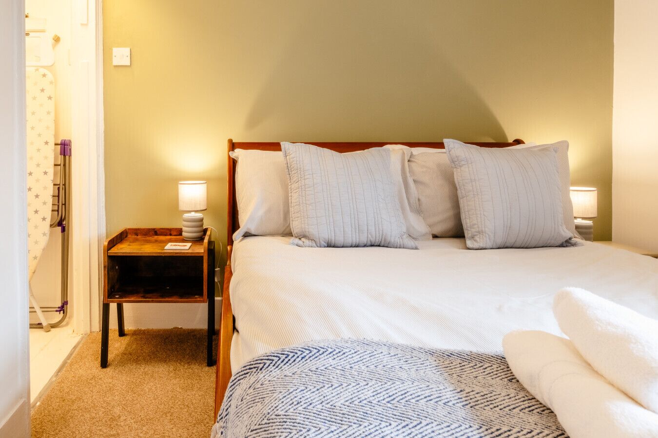 A neatly made bed with a wooden headboard, a bedside table with a lamp, and a patterned throw blanket.