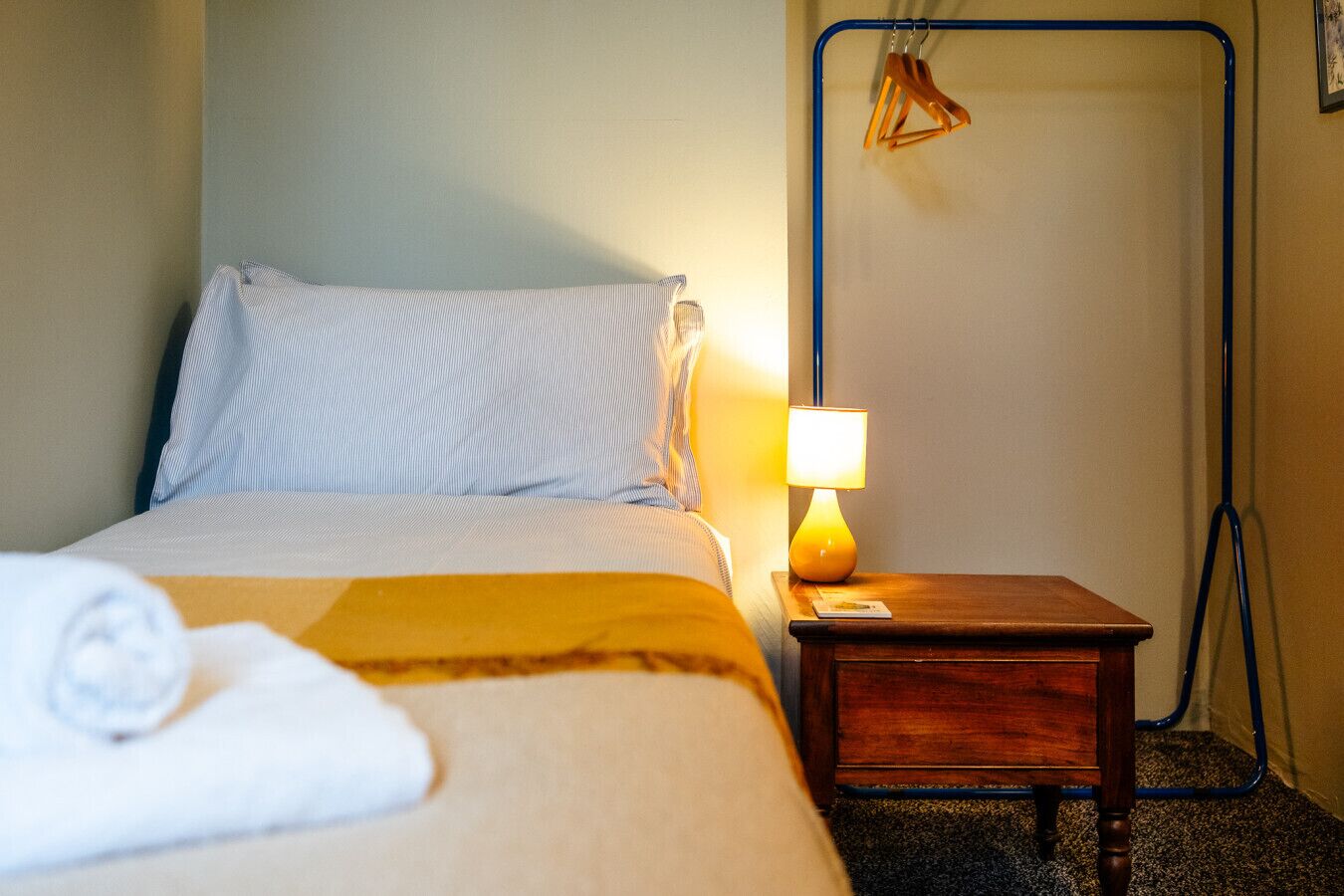 A neatly made bed with a striped pillow, a bedside lamp, and a wooden nightstand with a magazine.