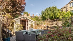Ein Steinhäuschen mit kleinem Garten und Terrassengarten, Korbmöbel und einem Holzzaun.