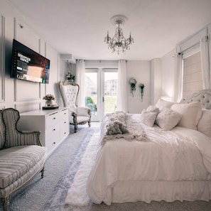 Ein Schlafzimmer mit einem großen Bett, einem an der Wand montierten Fernseher, einer Kristallleuchtreiter und Blick ins Freie.