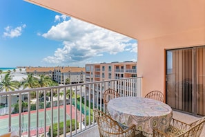 Enjoy the view of the tennis court and beach from this balcony with a table and wicker chairs.