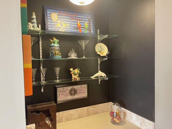 A bathroom with a shelf displaying various decorative items, a clock, and a sign with phrases. - Reef Club 503 - GULF FRONT! (Indian Rocks Beach)