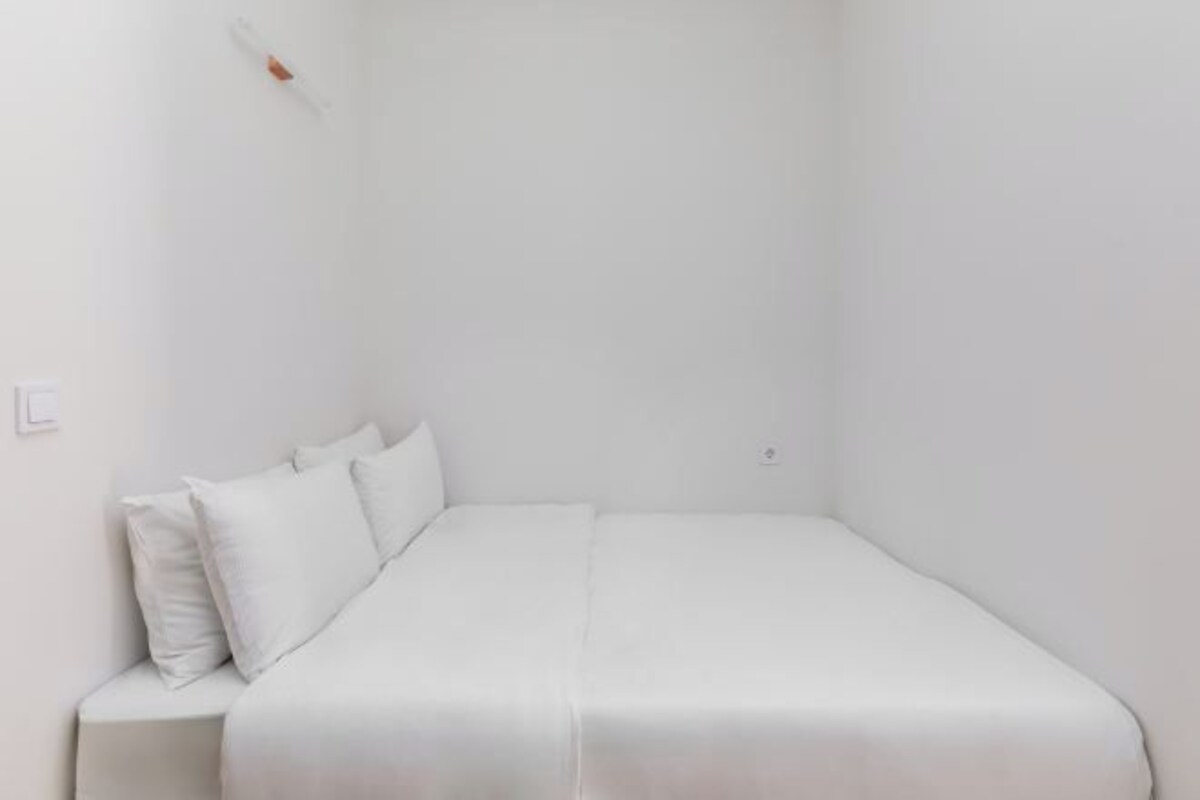 Una habitación pequeña con una cama individual, paredes blancas y un diseño sencillo, además de una mesita de noche.
