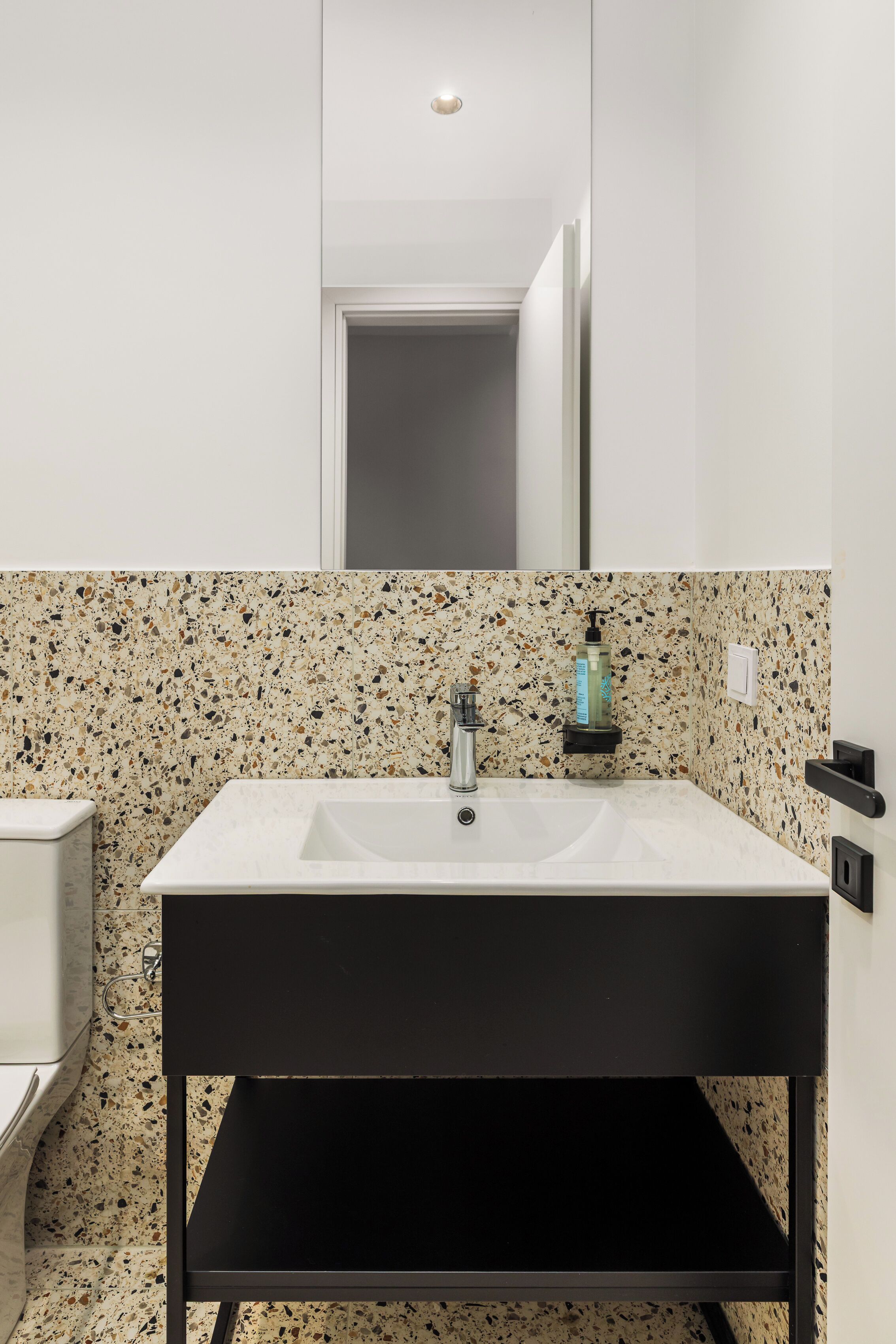 Un baño con lavamanos blanco, encimera negra y salpicadero de azulejos con motas.