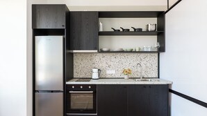 A modern kitchen with dark cabinetry, a stainless steel refrigerator, a built-in oven, and a granite countertop. - Soho Residence by halu! (Thessaloniki)