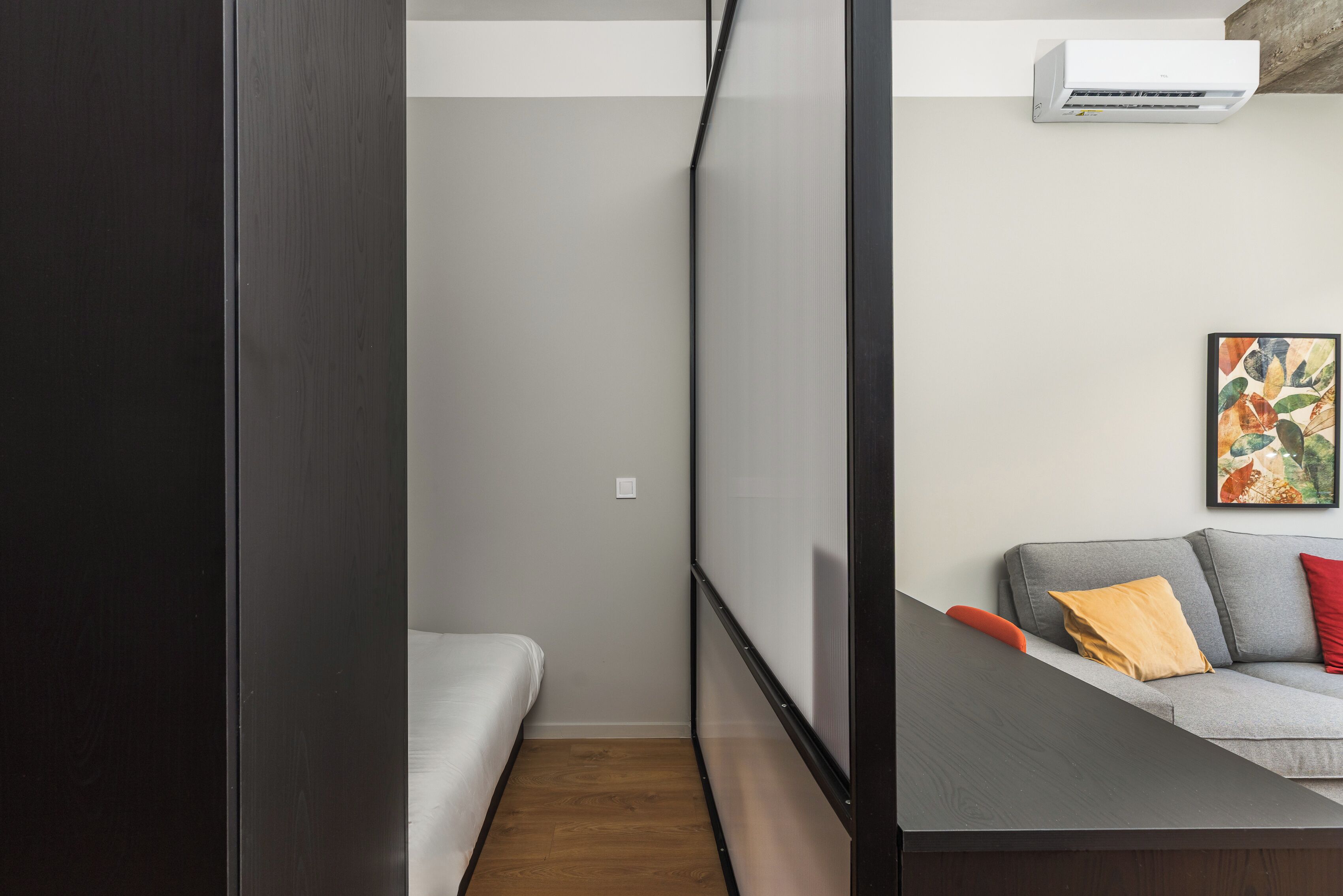 Una habitación moderna con una cama, un sofá gris con cojines y un equipo de aire acondicionado en la pared.