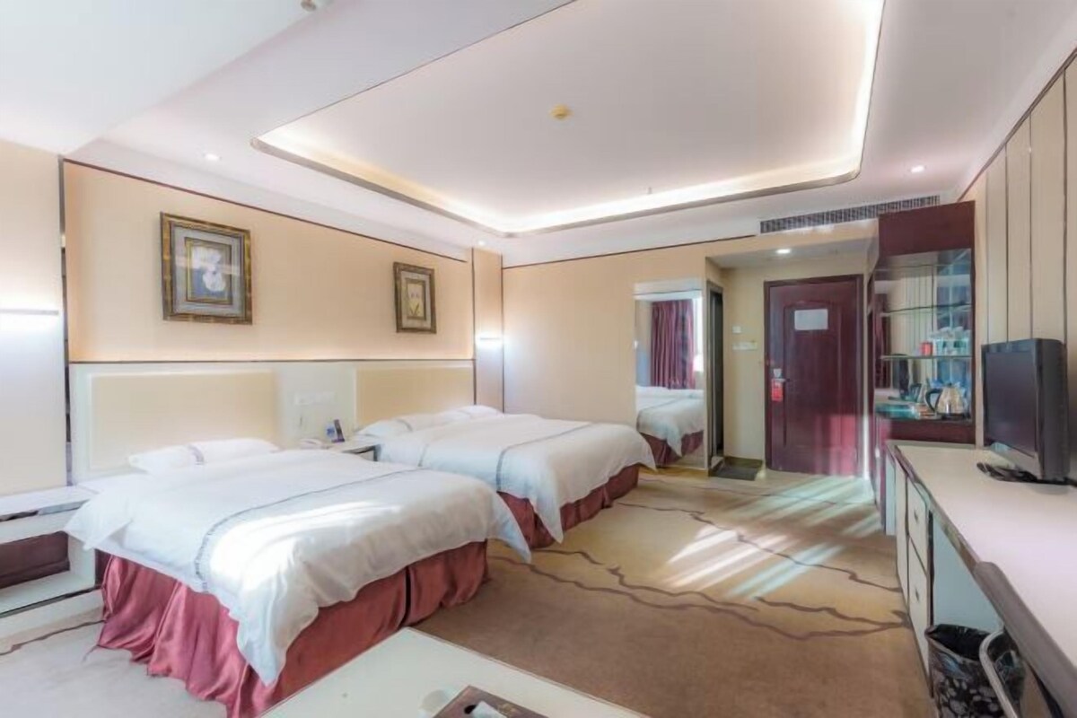 A hotel room with two beds, a TV, a desk, and a mirror.