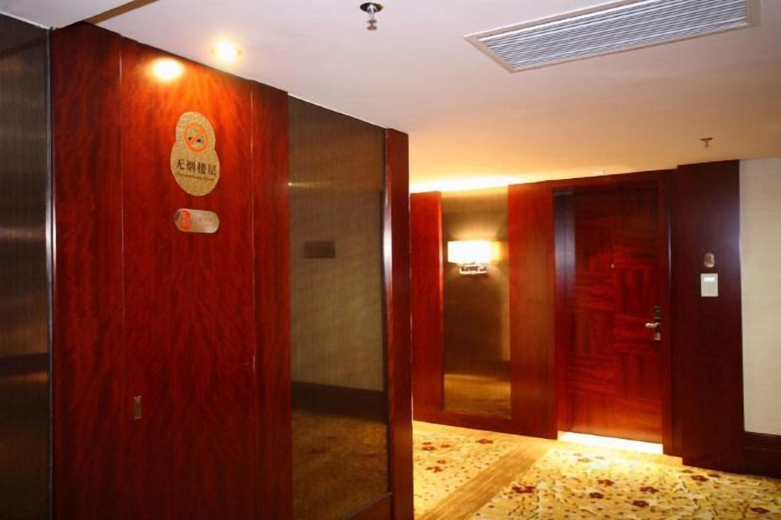 An interior corridor with wooden doors, a carpeted floor, and a wall-mounted light fixture.