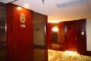 An interior corridor with wooden doors, a carpeted floor, and a wall-mounted light fixture. - Jin Yu Hotel (Zhuhai Gongbei Port Pedestrian Street) (Zhuhai)