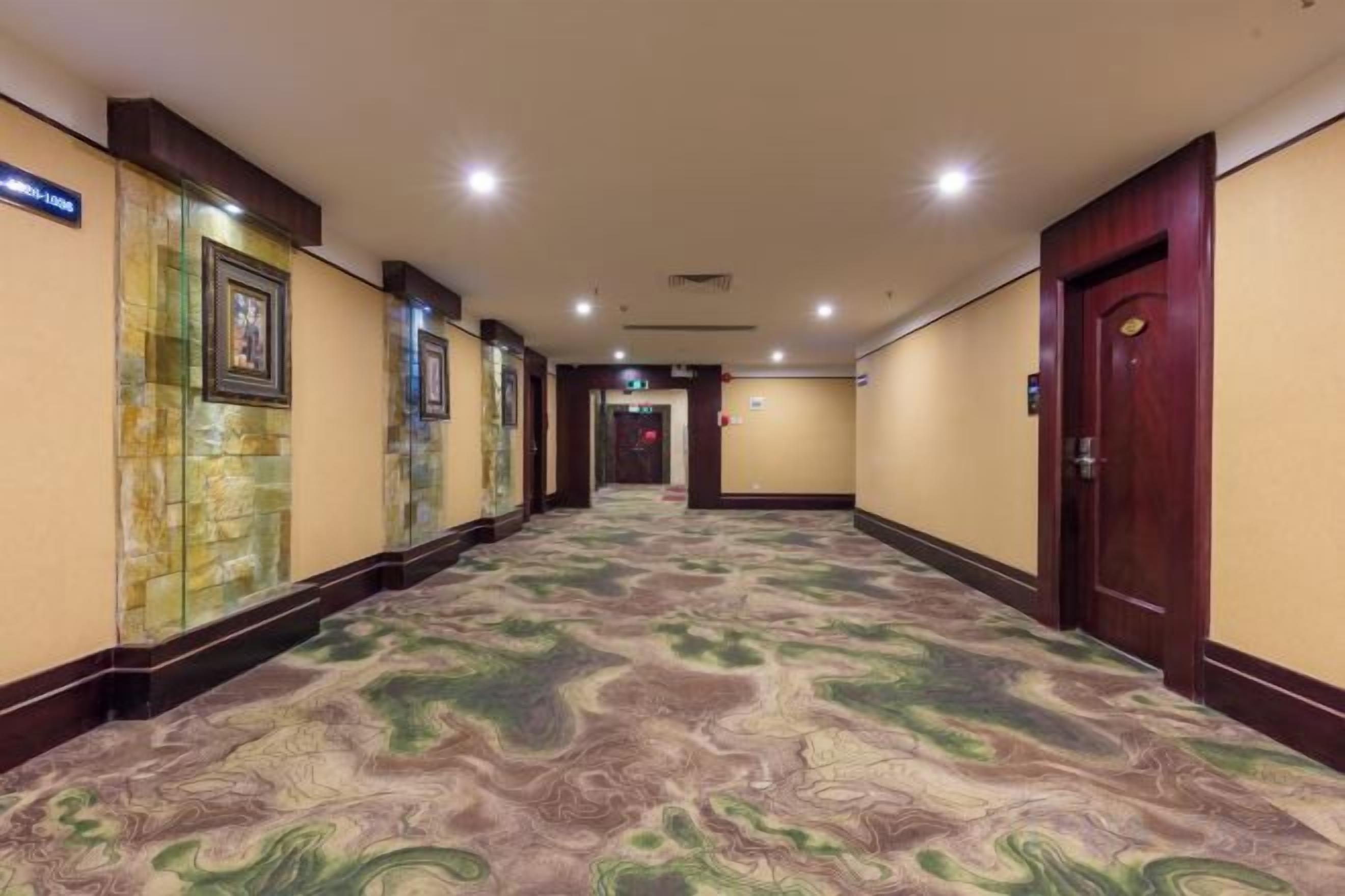 Un pasillo de hotel con alfombra estampada, obras de arte enmarcadas en las paredes y una puerta de madera al final.