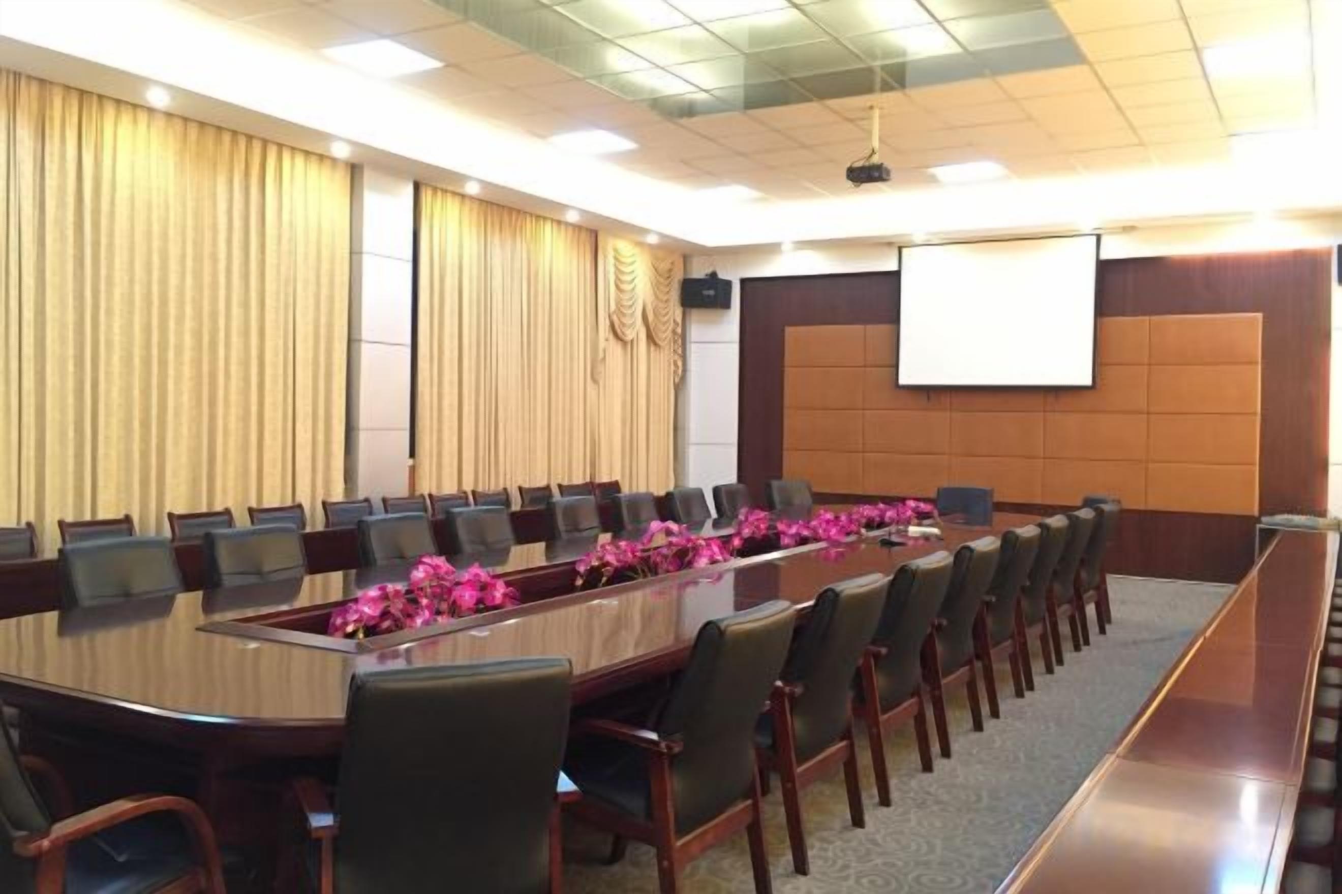 Une salle de conférence avec une longue table, des chaises, un écran de projection et un sol recouvert de moquette.