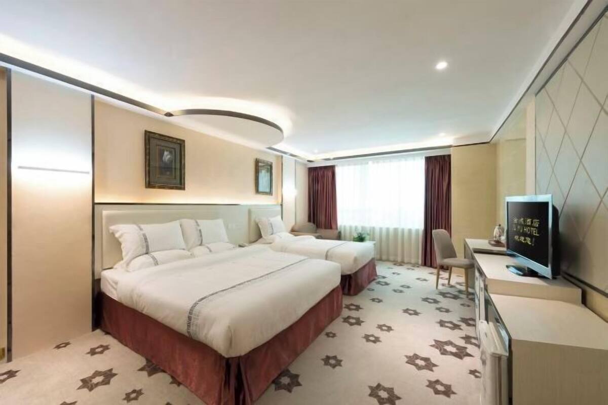 Habitación de hotel con dos camas, televisión, escritorio y un ventanal grande con cortinas.