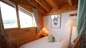 Een houten kamer met een bed, twee lampen, een stoel en een poster met de Olympische ringen.
