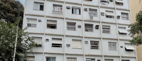Un edificio de varios pisos con numerosas ventanas, algunas abiertas o sin vidrios, y un número de puerta visible,