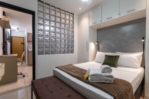 A modern hotel room with a large bed, a bench, a glass block wall, and a desk with a chair.