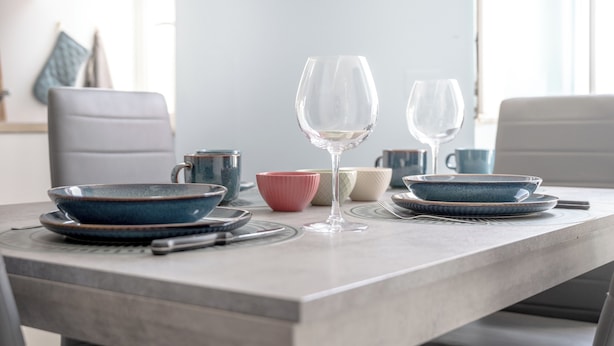 Una mesa de comedor con cuencos azules y rosados, una copa de vino y una taza.