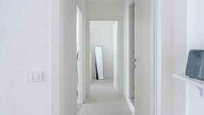 Un pasillo estrecho con paredes blancas y piso de tono claro, que lleva a una puerta al final.