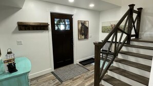 A spacious hallway with a wooden staircase, a black door, and a mounted artwork. - Escape to Luxurious Lynndyl Resort—Nature, Comfort & Serenity Await (Lynndyl)