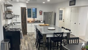 A modern kitchen with white cabinets, a black refrigerator, and a dining area with a wooden table and chairs. - Escape to Luxurious Lynndyl Resort—Nature, Comfort & Serenity Await (Lynndyl)