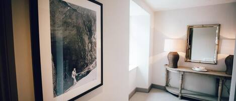 A hallway with a framed artwork on the wall, a console table with a mirror and decorative items, and a carpeted floor.