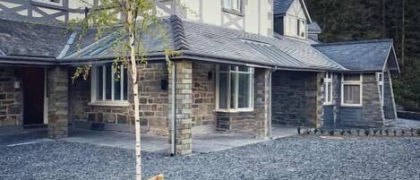 A two-story house with a stone facade, a sloped roof, and a gravel driveway.