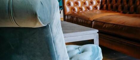 Une pièce avec un mur de couleur turquoise, un canapé en cuir marron et un fauteuil bleu.