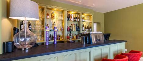 A bar area with a counter, shelves of bottles, glasses, and a barista station.