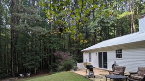 A house with a covered patio area, a lawn, and a dense forest in the background.