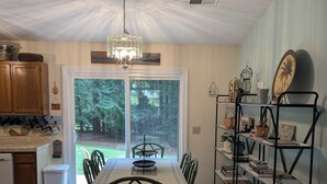A dining area with a table and chairs, a chandelier, a bookshelf, and a view of the outdoors.