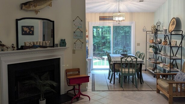 A living room with a fireplace, a dining area with a table and chairs, a bookshelf, and a view of the outdoors.