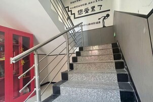 Un escalier avec une rampe métallique et une porte rouge sur le côté gauche.
