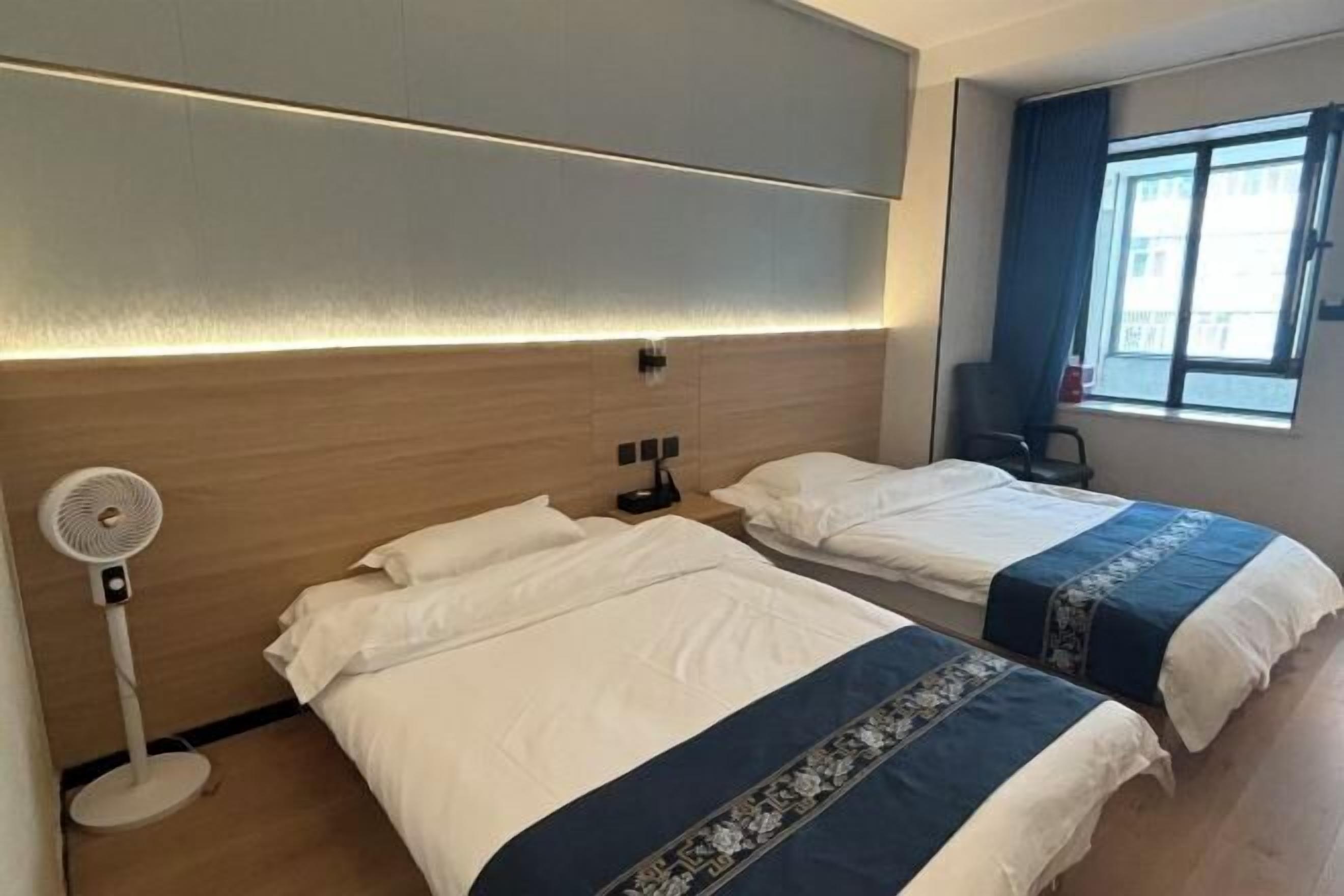 Habitación de hotel con dos camas, una mesita de noche, una lámpara, un ventilador y una ventana con cortinas.