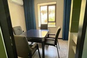 Een vergaderruimte met een tafel, vier stoelen, een raam met gordijnen en een airconditioner aan de muur.