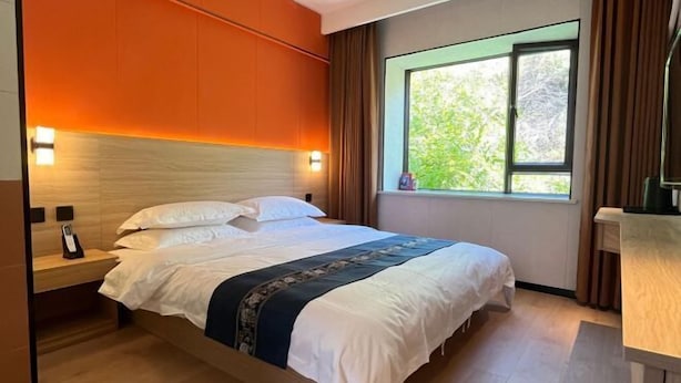 A hotel room with a bed, bedside table, and a window with curtains. - Altay Fenglinwan Boutique Hotel (Altay City)