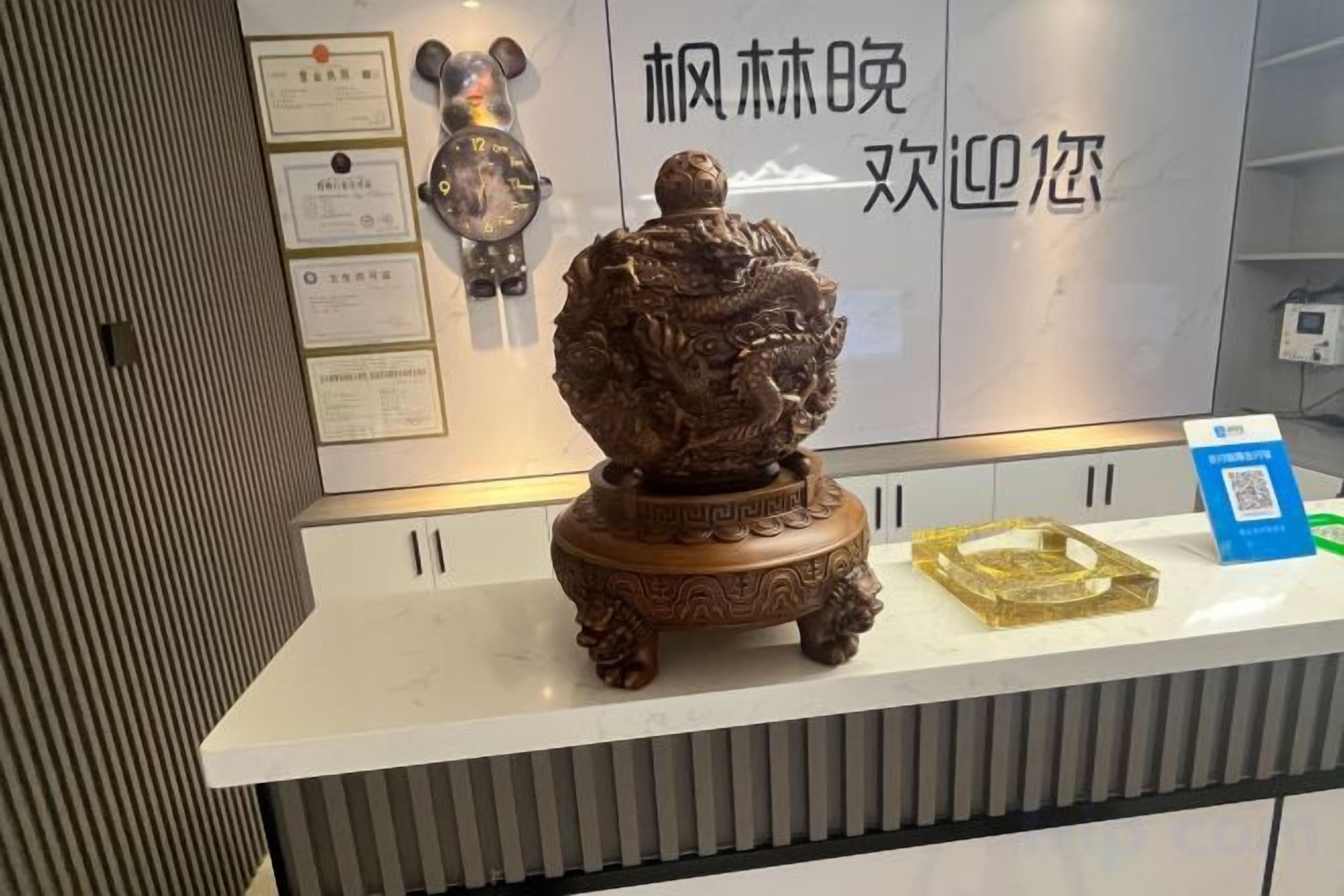 A reception desk with a decorative bronze statue, framed certificates, and a QR code on the counter.