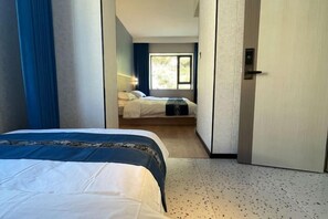 Habitación de hotel con una cama grande, una cama más pequeña al fondo, una ventana con vistas a zonas verdes y una puerta con cerradura.