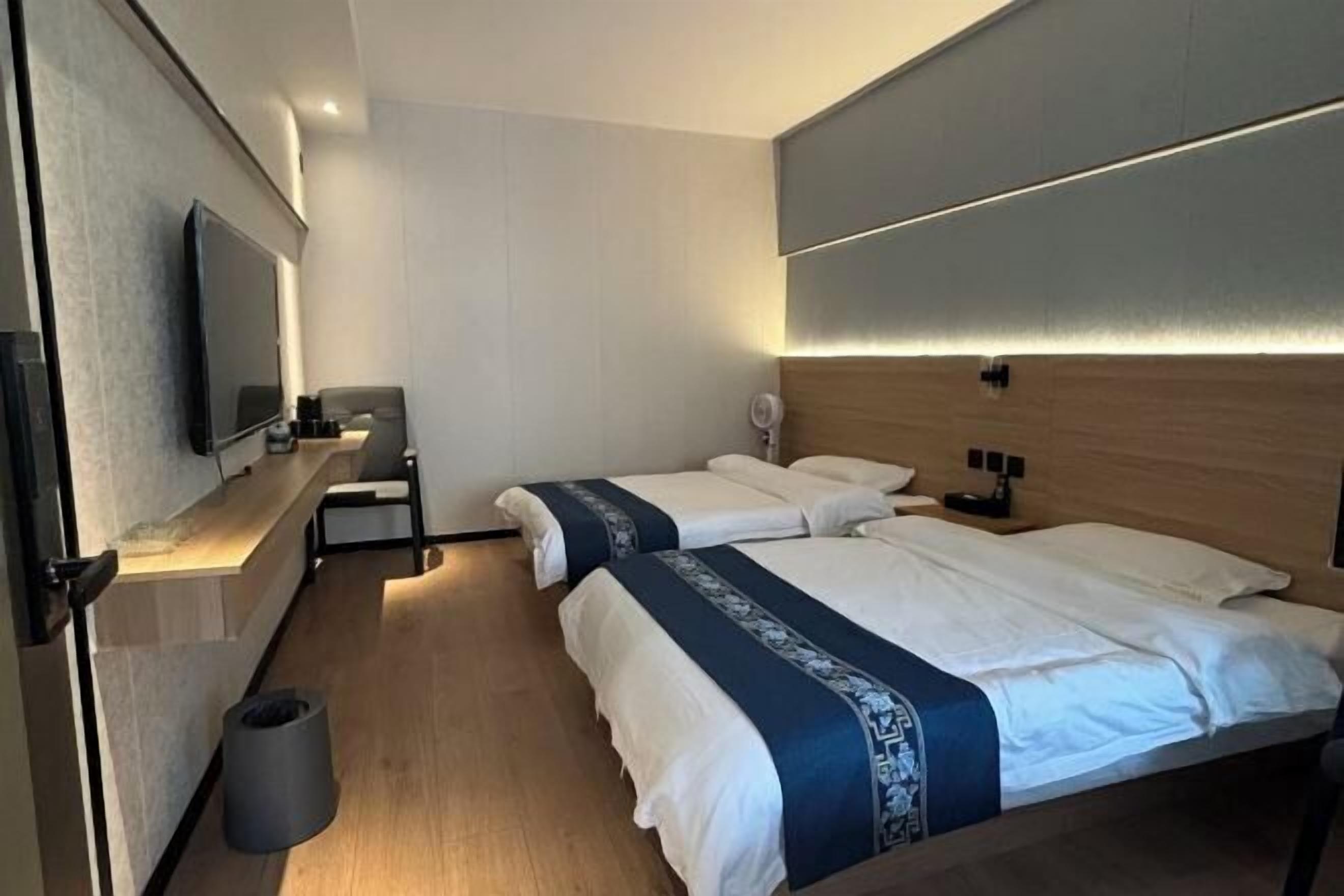 A hotel room with two beds, a TV, a small table, and a trash bin.
