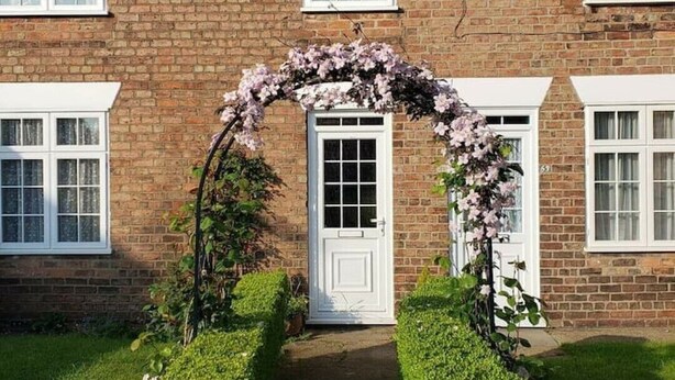 A brick house with a white door and a flower archway leading to a white door. - Lavender Cottage, a pretty period cottage in Louth (Louth)