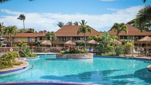 Una piscina de resort en un entorno tropical, con palmeras y sombrillas de paja.