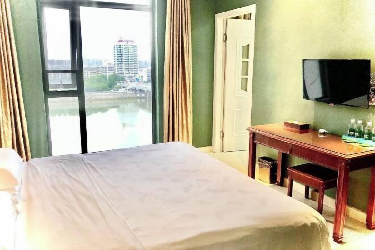Ein Hotelzimmer mit Bett, Schreibtisch, Fernseher und Blick auf ein Gewässer.
